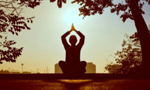 Silhouette d’une personne pratiquant le yoga en plein air au lever du soleil, dans une atmosphère apaisante.