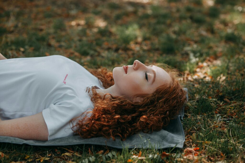 Adult woman with red hair doing yoga nidra in Etterbeek on a sunny day, surrounded by nature in relaxation